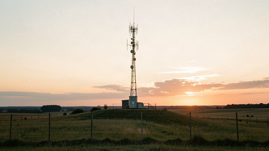 Documentary photograph of a rural Missouri radio communications tower on a grassy hilltop at golden hour, wide shot showing antenna arrays and open Midwestern farmland