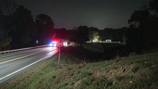 Rural two-lane Missouri highway at night with distant blurred red and blue emergency lights