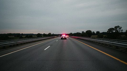 Empty New Jersey Turnpike at dusk with a distant state police cruiser far down the road, overcast sky, documentary news photograph