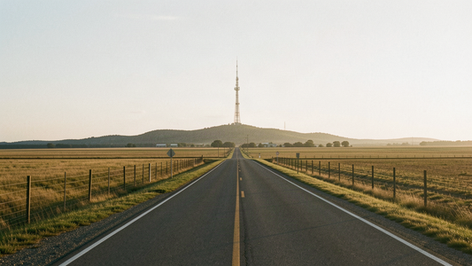 A rural Oklahoma county road at golden hour leading to a distant radio tower as Kingfisher County law enforcement and fire dispatch go encrypted in August 2026
