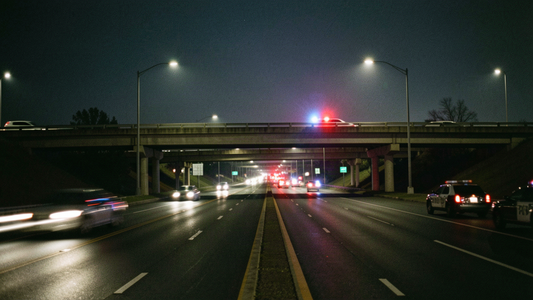 Empty closed lanes of a suburban freeway interchange at night with distant blurred emergency lights